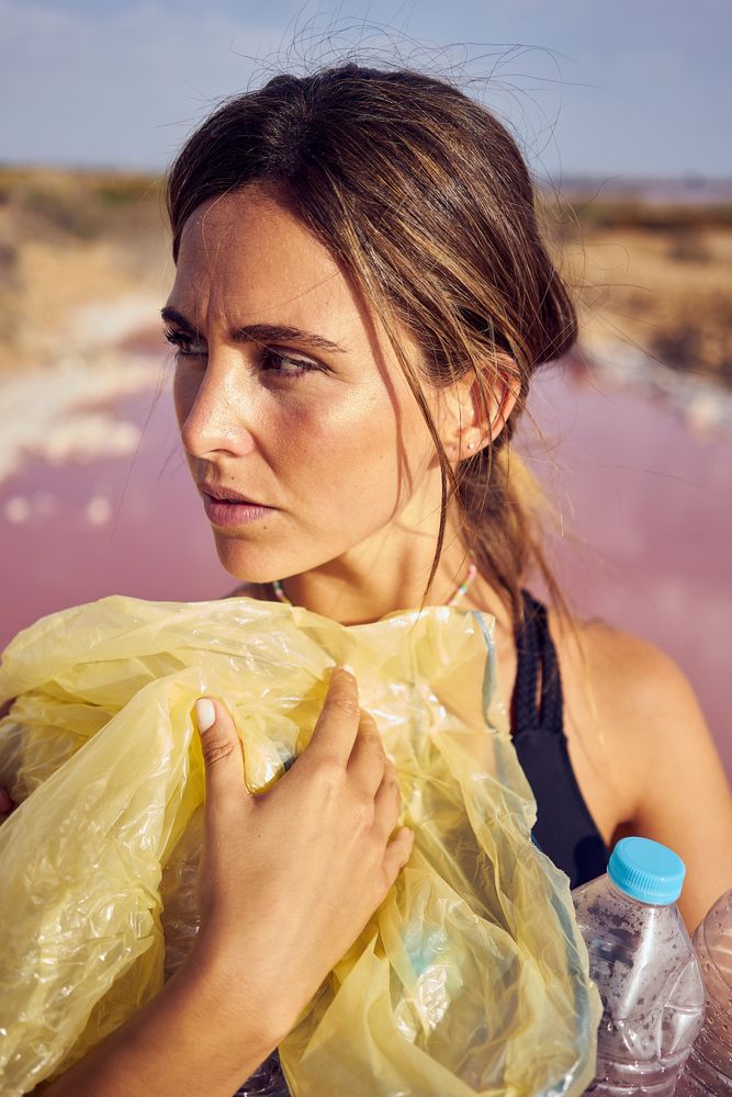 Concerned female in swimsuit collecting trash in natural lake