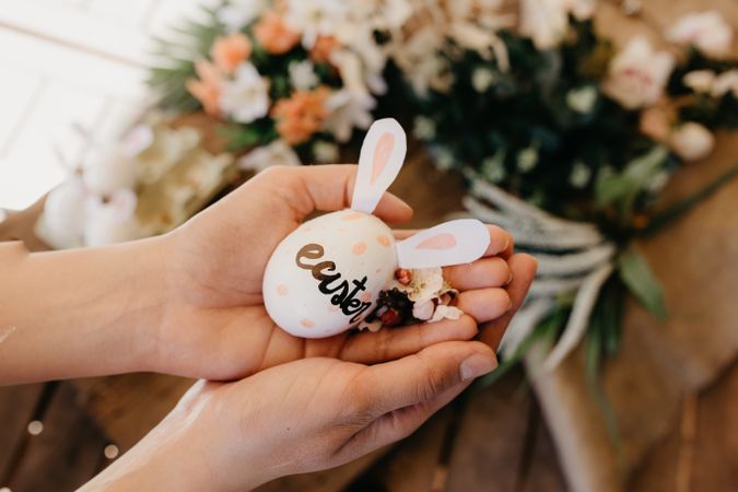 young woman holding an easter egg with rabbit ears painted by children with flowers