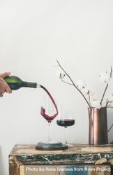 Wine glasses being poured from bottle with dried cotton in vase, vertical composition, copy space bEEDNb
