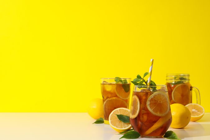 Cold tea with orange slices and mint leaves on a yellow background