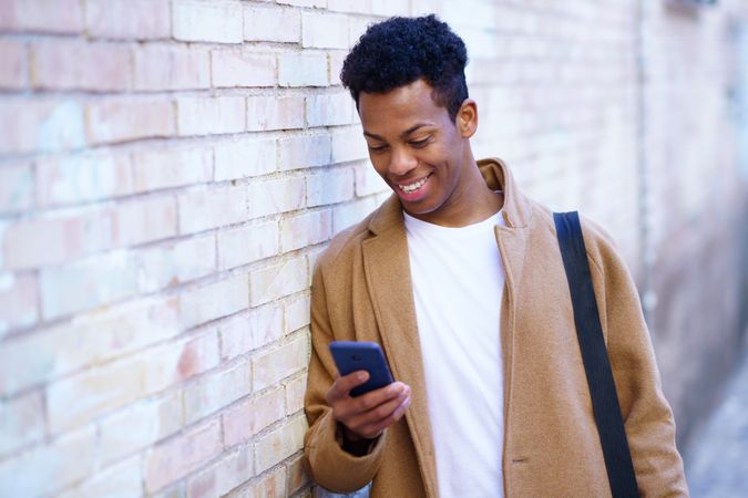 Smiling Cuban male leaning against wall looking down at his phone