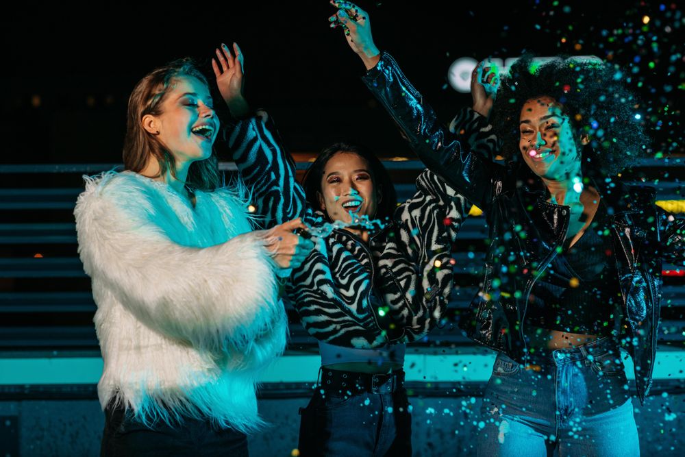 Multi-ethnic group of woman celebrating with confetti opening champagne bottle