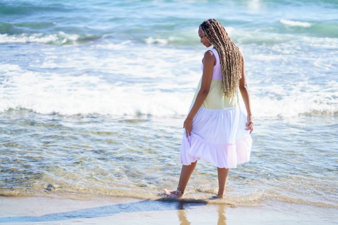 Barefoot Black woman walking through the water at beach in colorful dress
