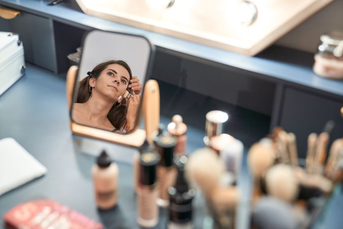 Faceless visagiste applying makeup on woman reflecting in mirror