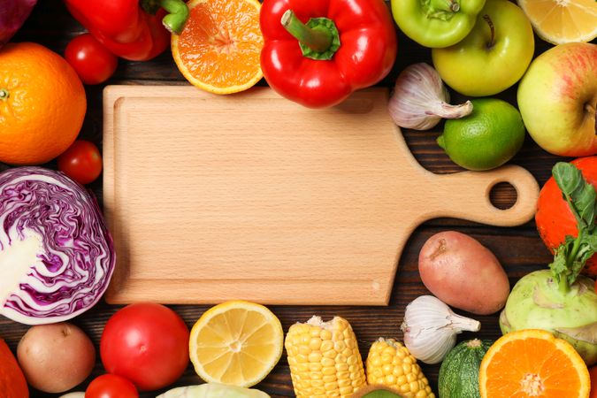 Board and different vegetables and fruits on wooden background, top view