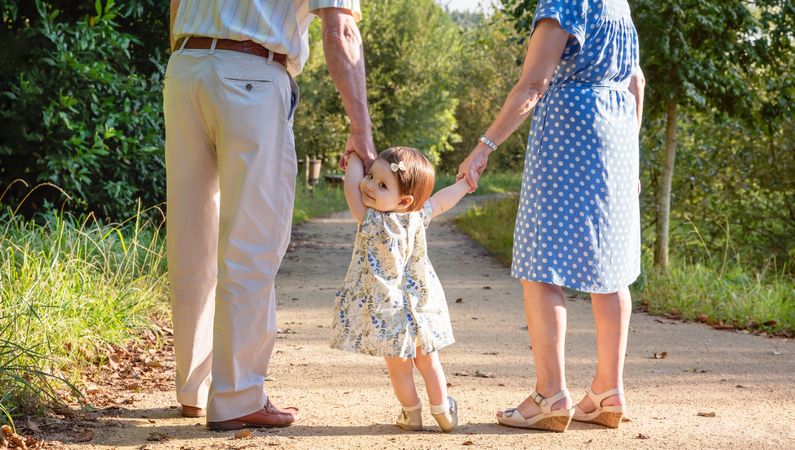 Baby granddaughter walking with her grandparents outdoors