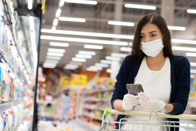 Woman checking list on her smart phone at grocery store wearing surgical mask