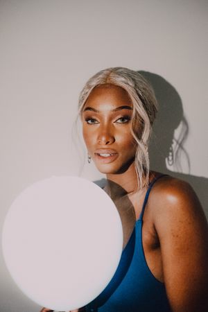 Black adult woman with illuminated balloon in darkness looking at camera