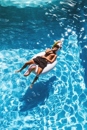 Man lying on an inflatable unicorn floating on swimming pool