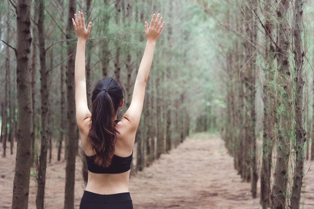 Woman stretching arms up working out in forest