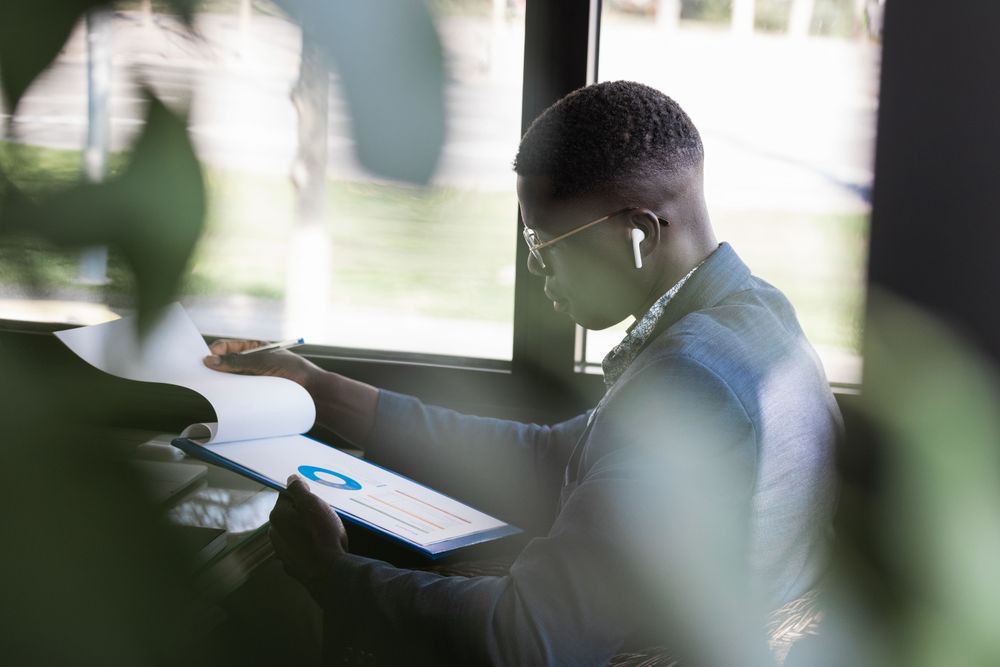 Serious Black businessman in earbud with diagram on paper indoors
