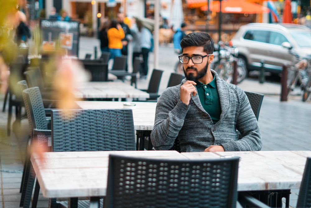 Man in gray sweater wearing eyeglasses sitting on dining table outdoor