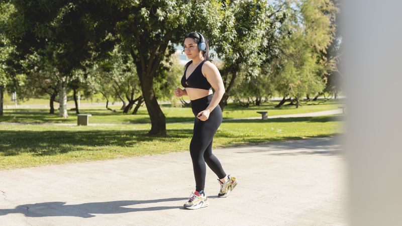 A concentrated young woman listens to music with headphones before starting a run in the park.