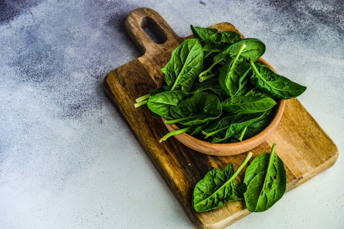 Wooden bowl of fresh spinach on kitchen counter with copy space