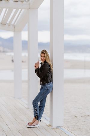 Smiling trendy woman leaning on white pillar on seashore