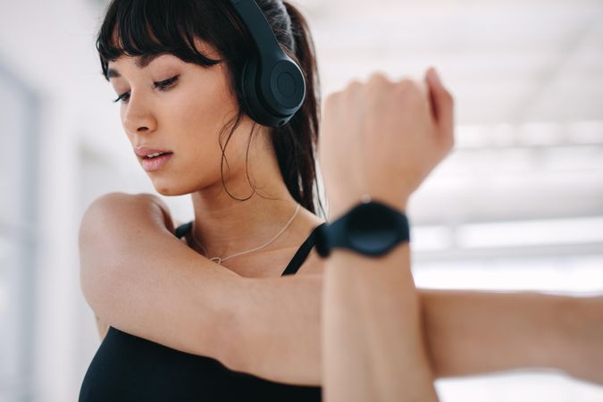 Close up of woman with headphones on stretching her hand at gym