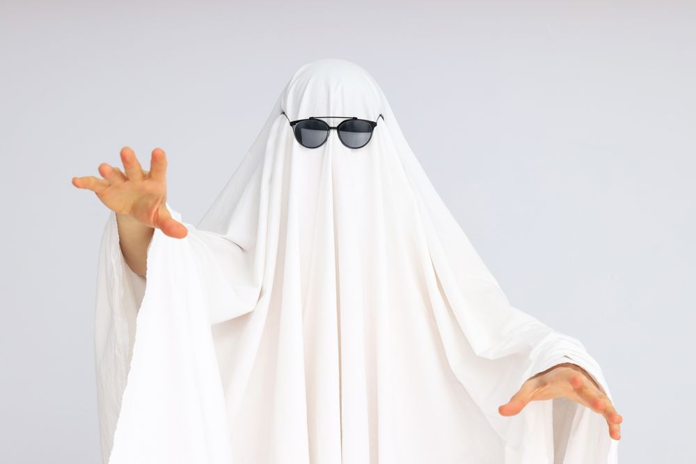 Concept of Halloween, woman in ghost costume and sunglasses on light background