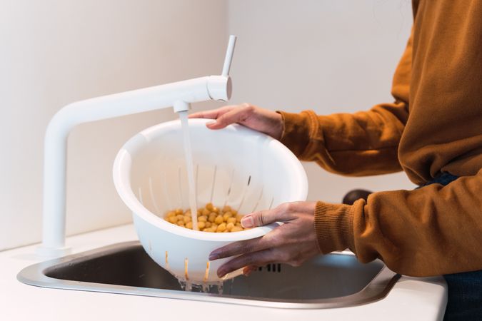 Crop woman washing chickpeas in sink