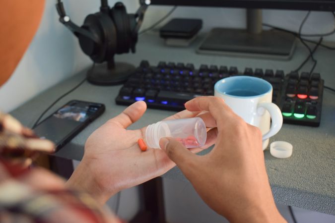Person sitting at desk pouring medication into palm of hand