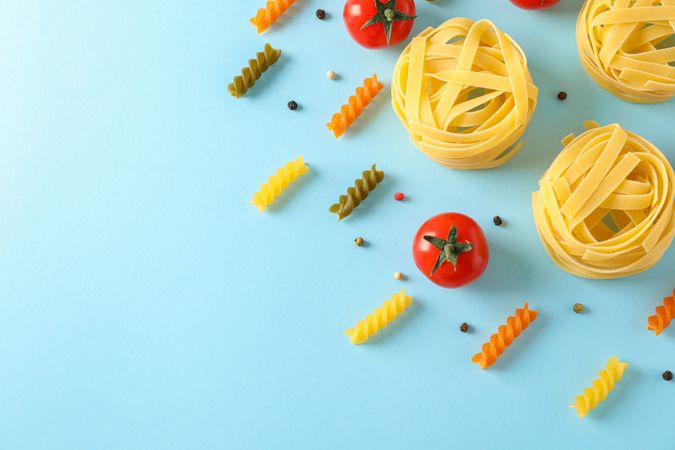 Flat lay composition with different pasta and tomatoes on color background, space for text. Dry uncooked whole pasta