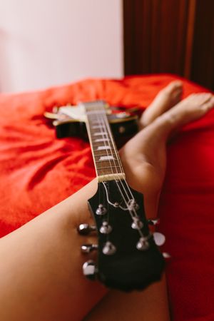 Crop female musician with electric guitar on bed