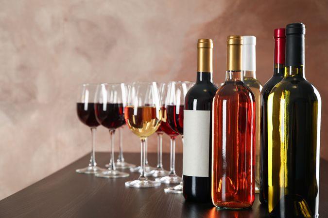 Bottles and glasses with wine against brown background, copy space