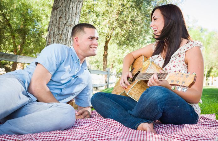 Woman Playing Guitar with Boyfriend In The Park.