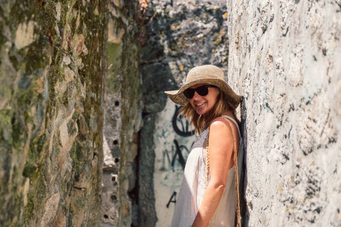 Woman in hat leaning in stone wall