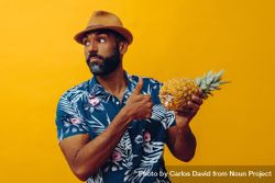 Male holding a pineapple to his chest with thumbs up sign in yellow studio 5QpRe0