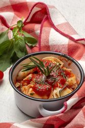Bowl of delicious ravioli with tomato sauce and rosemary on table cloth