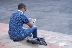 Rear of male sitting on stairs on sunny day and using tablet