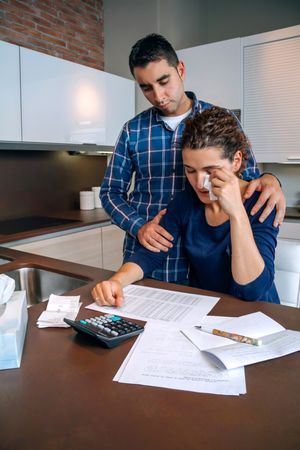 Sad couple reviewing bills together in the kitchen with wife crying, vertical