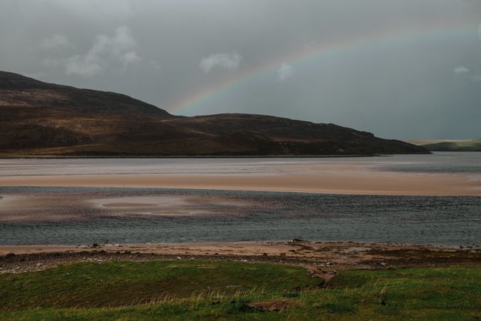 Dim rainbow over Scottish coast at sunset