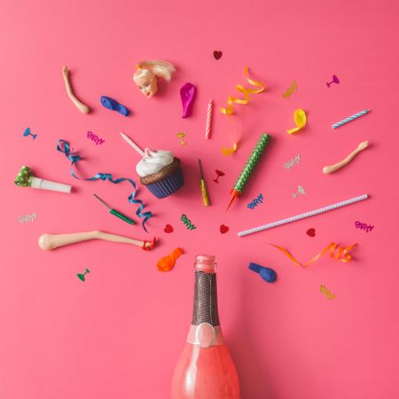 Champagne bottle with colorful party items on pink background
