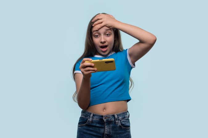 Girl looking shocked, holding smartphone, expressing surprise
