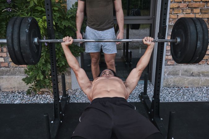White man lifting barbell with trainer