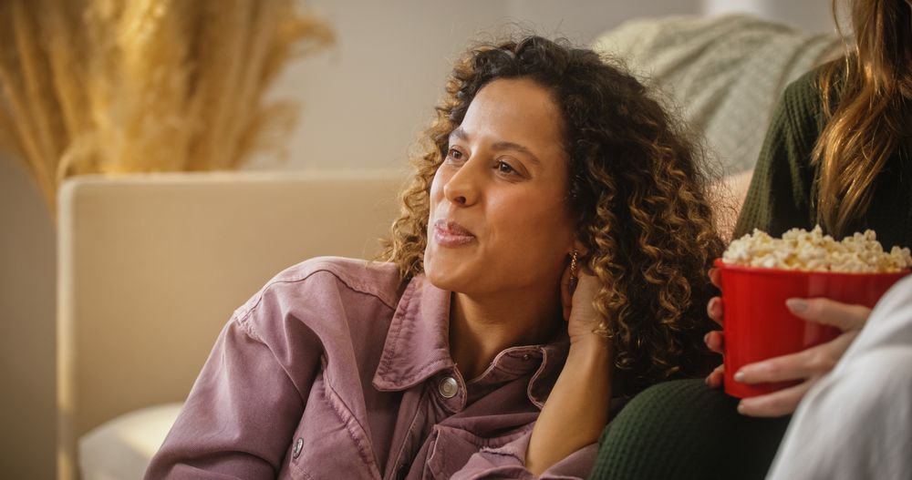 Portrait of Multiethnic Woman Watching a Funny Show with Friends and Laughing in Cozy Living Room.