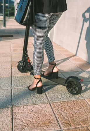 Unrecognizable businesswoman legs with e-scooter outdoors
