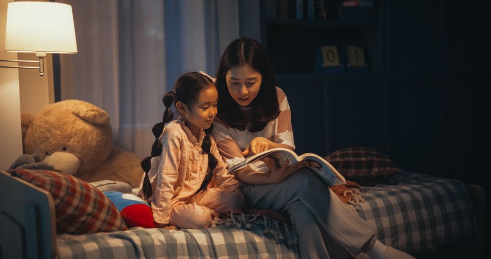 Korean Mom Caring for Little Girl, Reading Stories from a Book in the Evening at Home