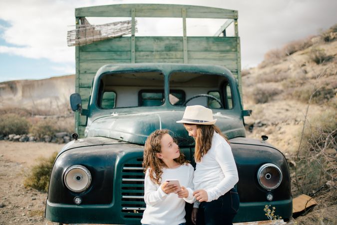 Cheerful girls watching smartphone near abandoned truck