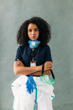 Serious medical professional holding goggles with hazmat suit and arms crossed