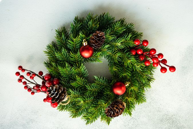 Christmas wreath with red baubles, pine cones and holly on marble counter