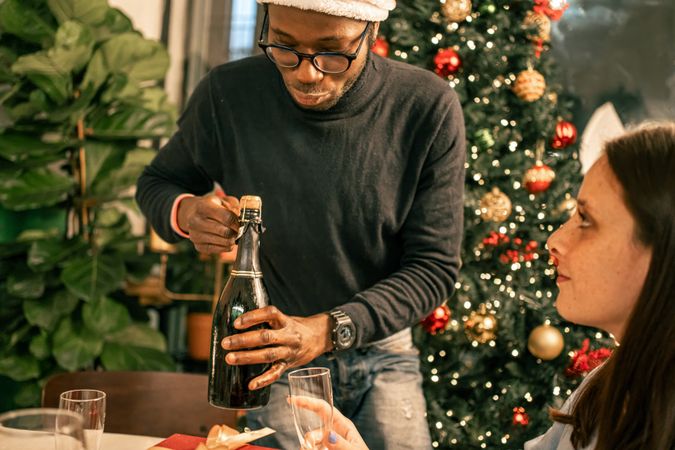 Diverse friends celebrating Christmas opening a bottle of sparkling wine at home.