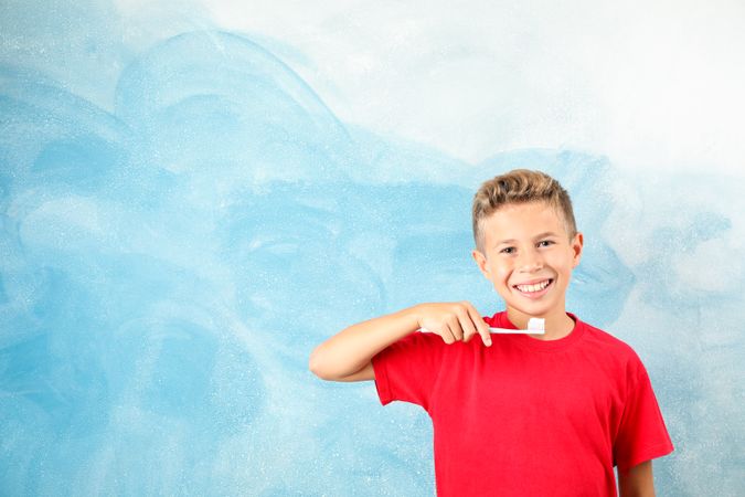 Boy with toothbrush on color background, space for text