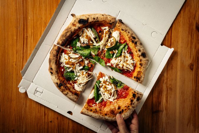Fresh gourmet pizza with cheese, spinach, tomato, crust, and sauce in a takeout box