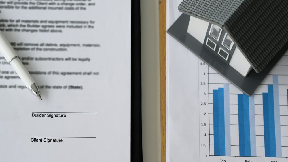 Pen placed on contract documents and model houses on data graphs