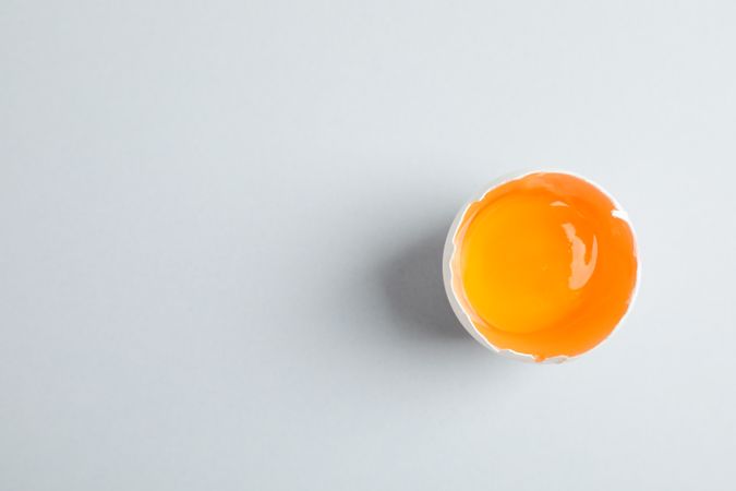 Half broken egg with yolk on grey background, space for text and top view