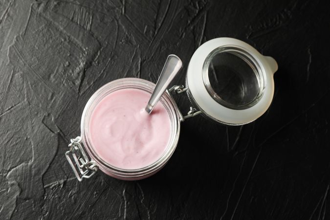 Glass jar with fruit yogurt on dark cement background, space for text