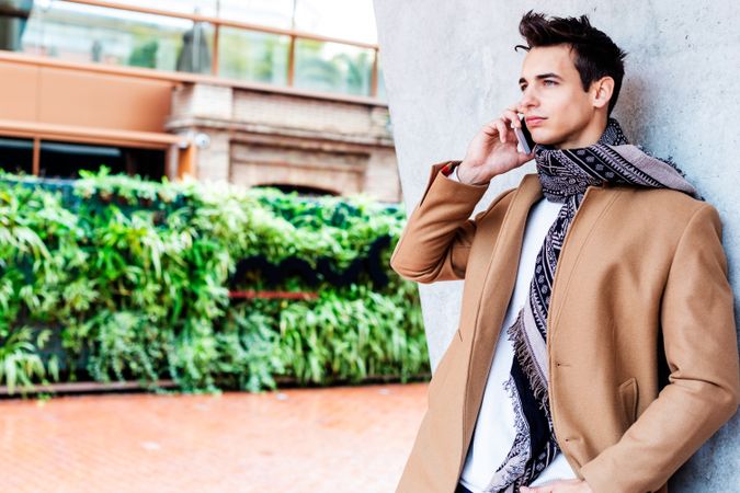 Male in camel coat and scarf standing outside talking on phone