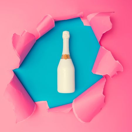 Torn pink paper revealing champagne bottle underneath on blue background